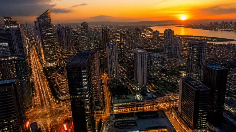 Cena aérea de uma cidade fictícia ao entardecer representando a evolução urbana de um mundo de jogo