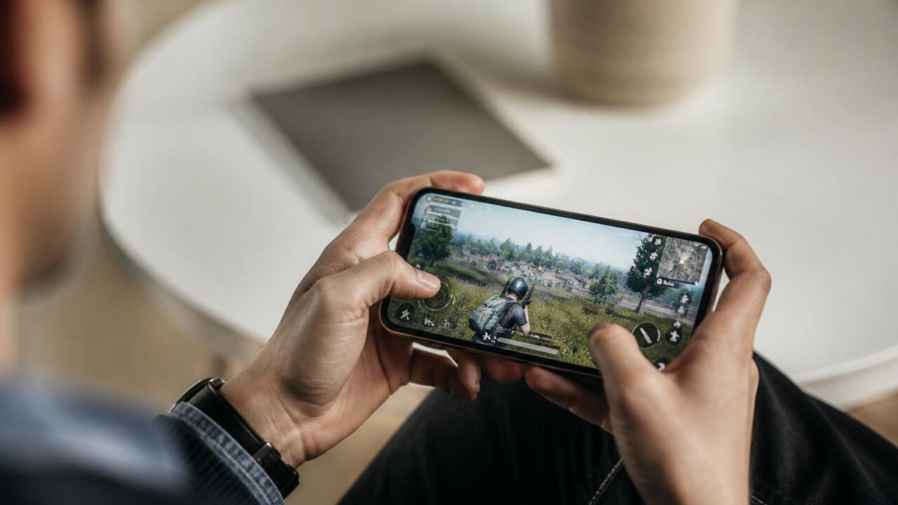 Proximidade de mãos segurando um smartphone com interface fictícia de jogo exibida na tela